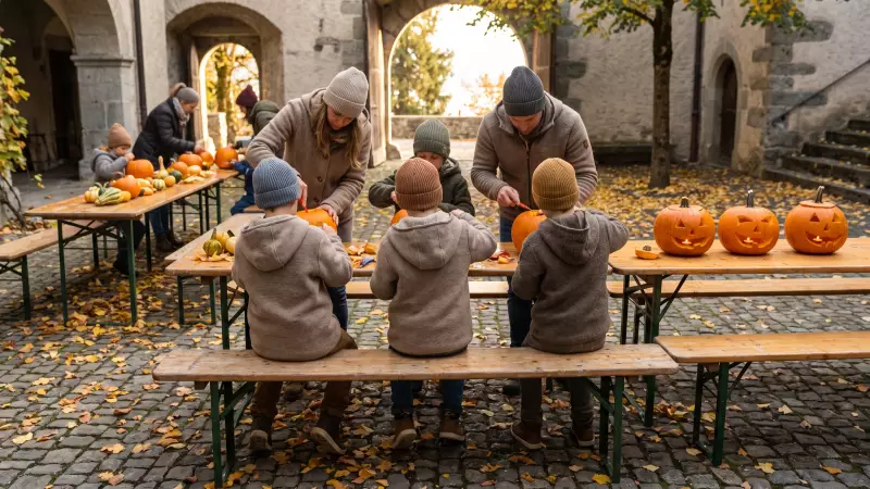 Des enfants vus de dos sculptent des citrouilles sur de longues tables en bois dans la cour d’un château, entourés de courges colorées
