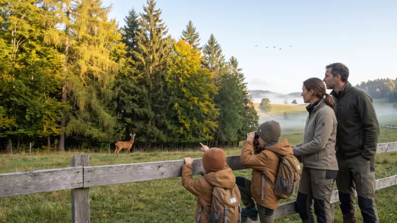 Deux enfants observent aux jumelles un chevreuil en lisière de forêt avec leurs parents, un matin brumeux de septembre en Suisse romande