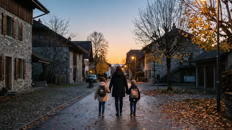 Parent et deux enfants rentrant de l’école vus de dos, dans une rue bordée d’arbres d’automne au coucher du soleil, illustration IA