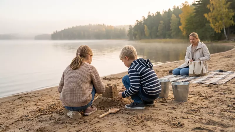 Deux enfants construisent un château de sable au bord d’un lac à la fin de l’été, vus de dos